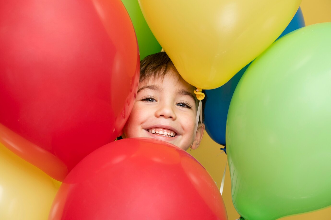 Niño sonriendo en su cumpleaños rodeado de globos.